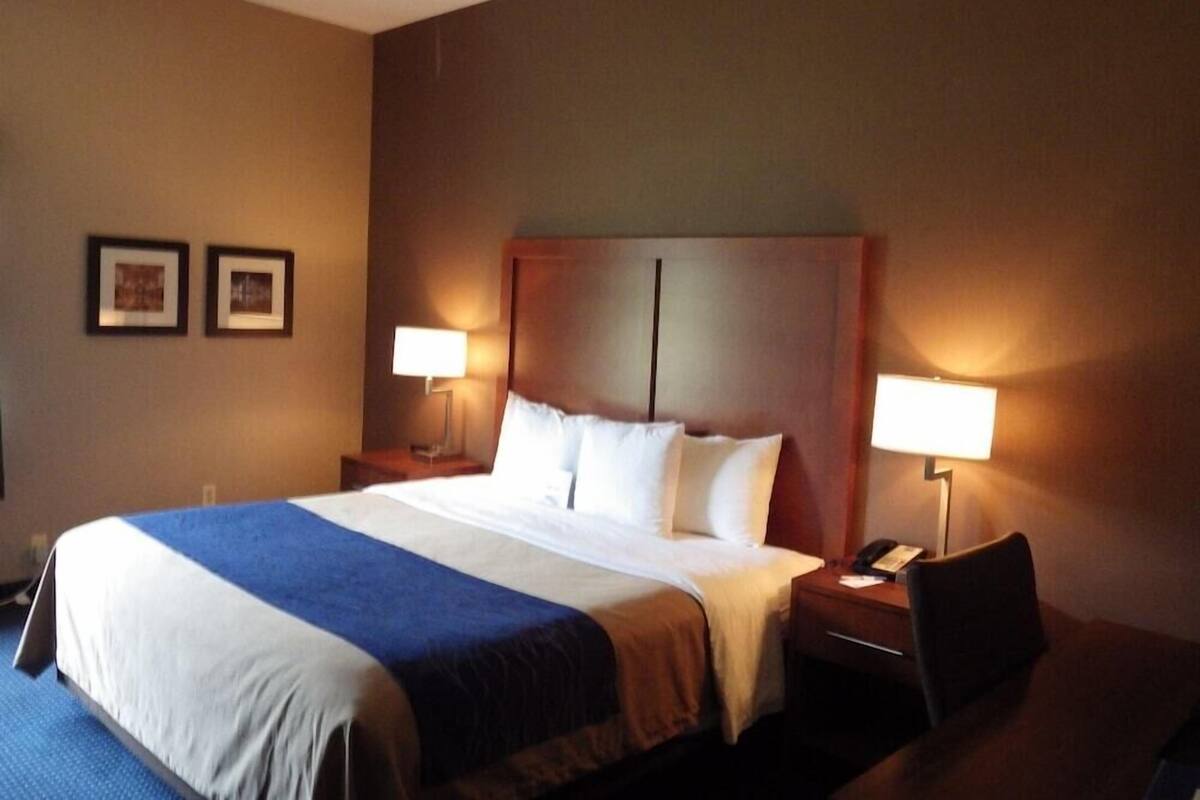 A hotel room with a large bed, two bedside tables, a desk, and two lamps.