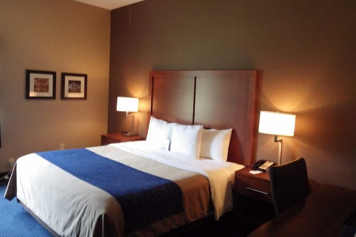 A hotel room with a large bed, two bedside tables, a desk, and two lamps.