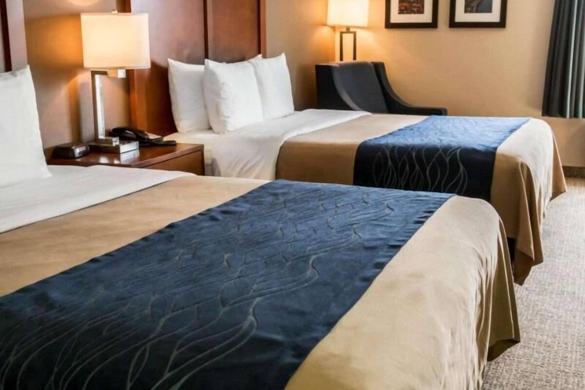 A hotel room with two beds, a wooden headboard, bedside lamps, a desk with a phone, and framed pictures on the wall.