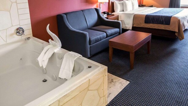A hotel room with a bathtub, two beds, a sofa, a small table, and two wall-mounted lamps. - Comfort Inn Crystal Lake - Algonquin (Crystal Lake)
