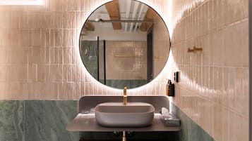 Een badkamer met een ronde spiegel, een wastafel met een gouden kraan en een handdoekrek.