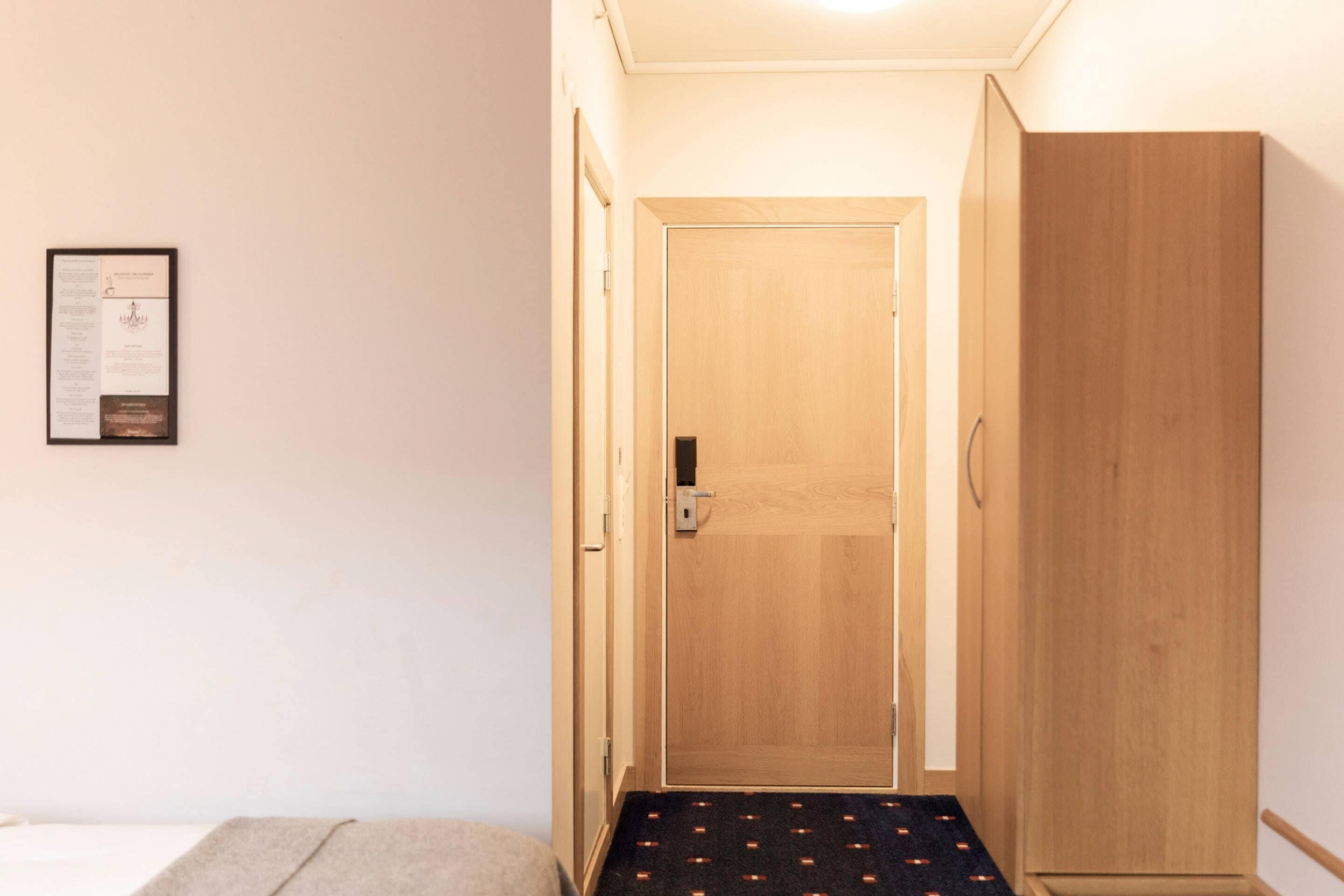 Un pasillo con puerta de madera, un certificado enmarcado en la pared y suelo alfombrado.