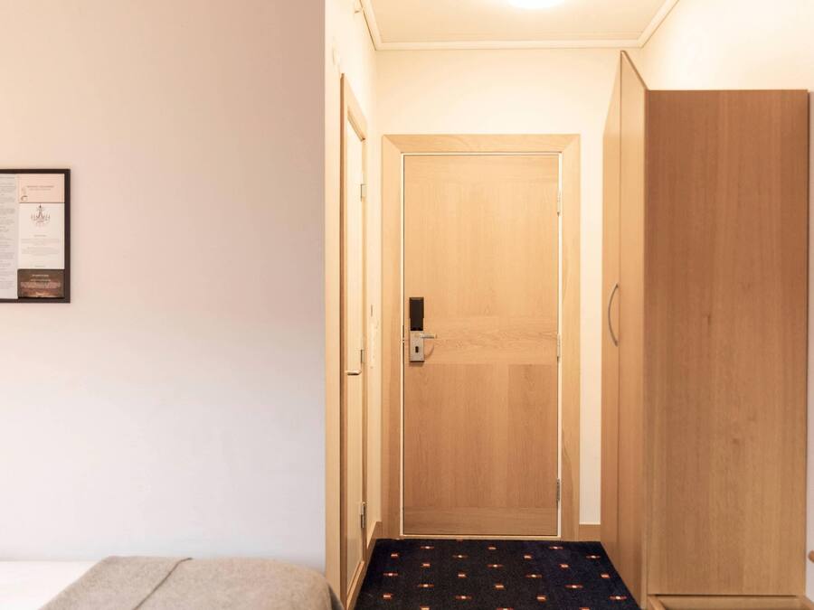 A hallway with a wooden door, a framed certificate on the wall, and a carpeted floor.