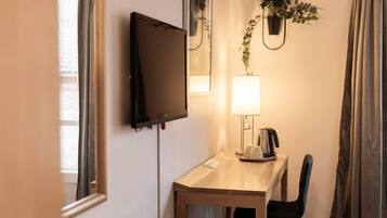 Een hotelkamer met een bureau, stoel, televisie, lamp en potplanten.