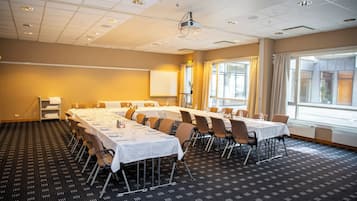A conference room with multiple tables set for dining, a projector on the ceiling, and large windows with curtains.