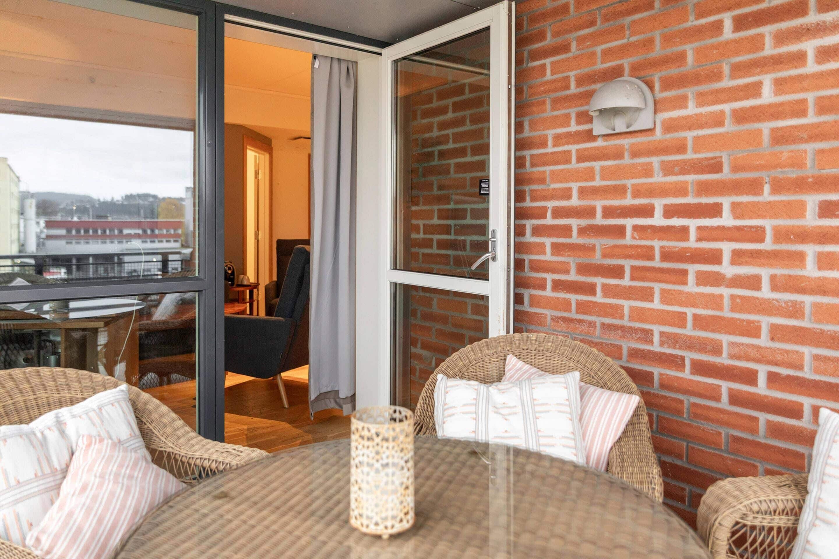 Ein Balkon mit Korbmöbeln, einem Glastisch und einer Ziegelwand.