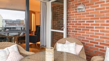 Ein Balkon mit Korbmöbeln, einem Glastisch und einer Ziegelwand.