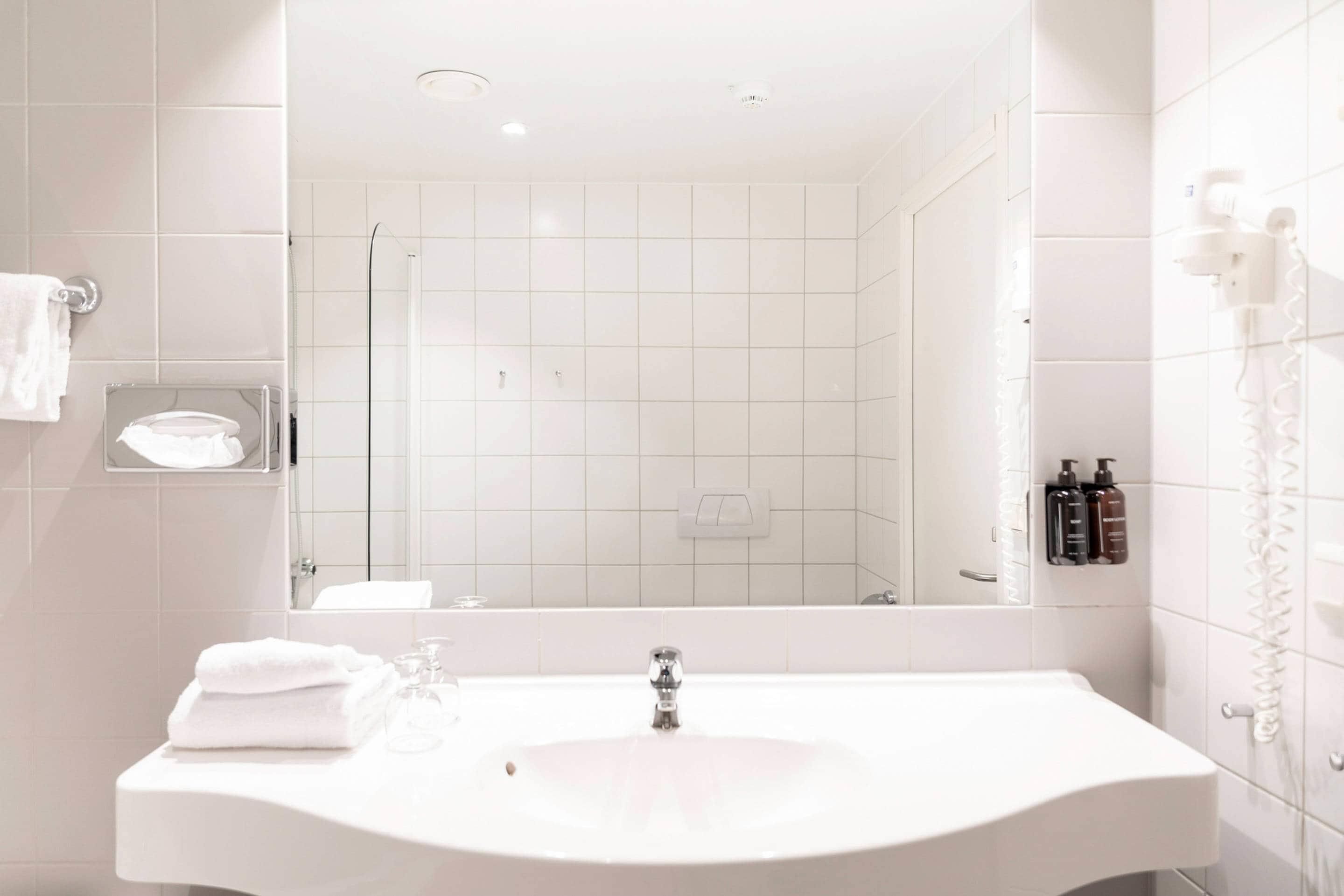 Ein Badezimmer mit einem weißen Waschbecken, einer Duschkabine aus Glas und einem Spiegel.