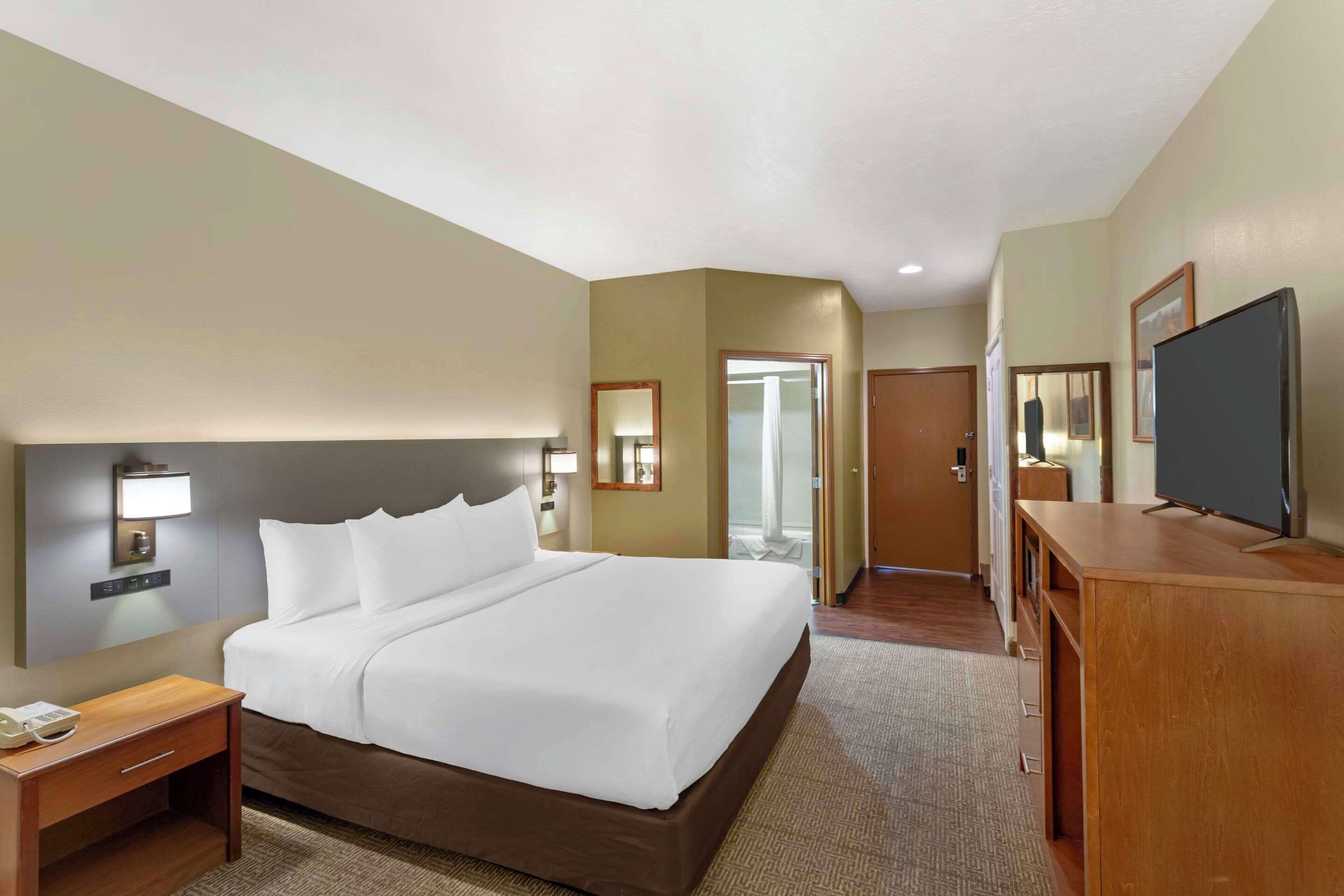 A hotel room with a large bed, bedside tables, a desk, a television, and a door leading to a bathroom.