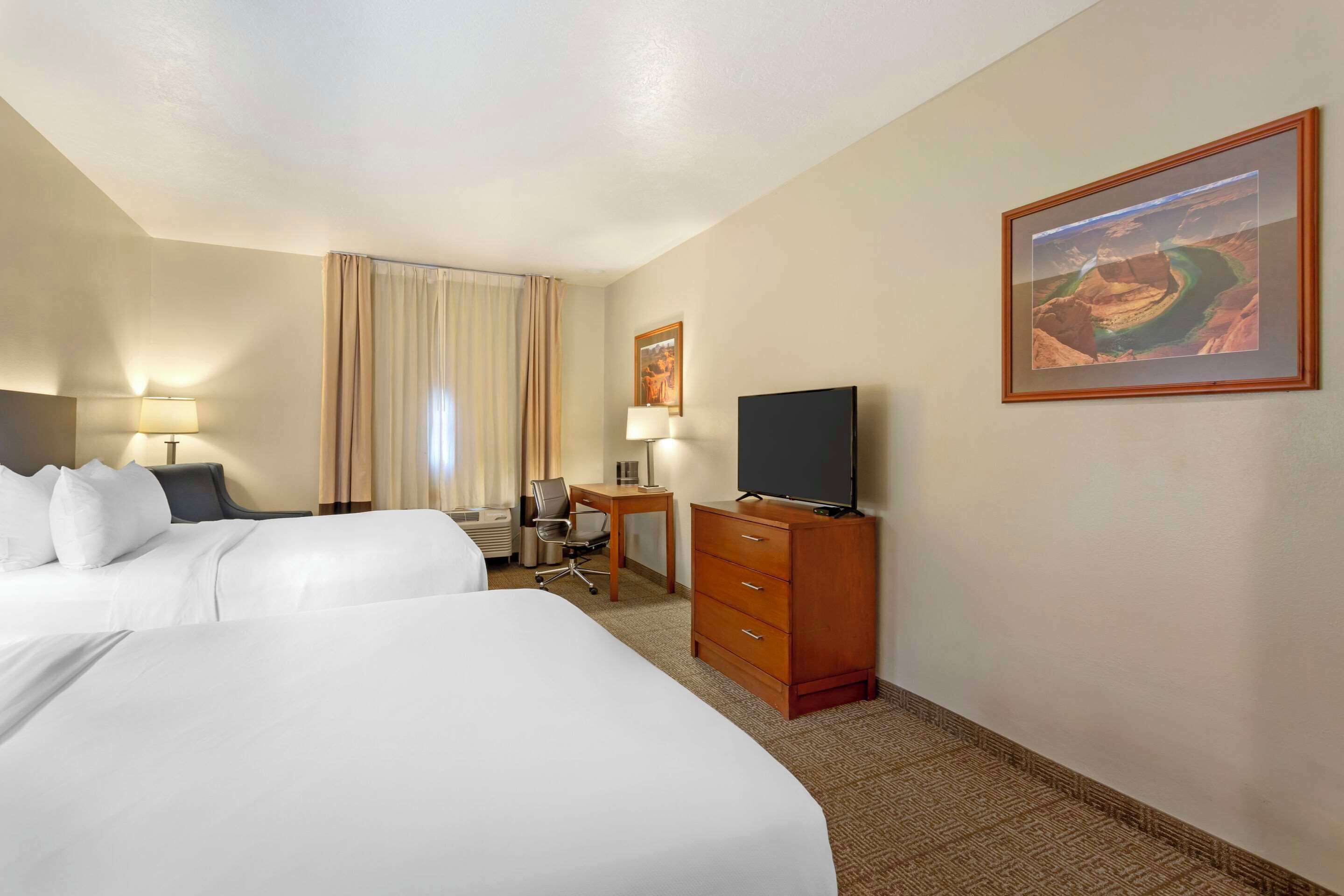 A hotel room with two beds, a desk, a TV, and a painting on the wall.