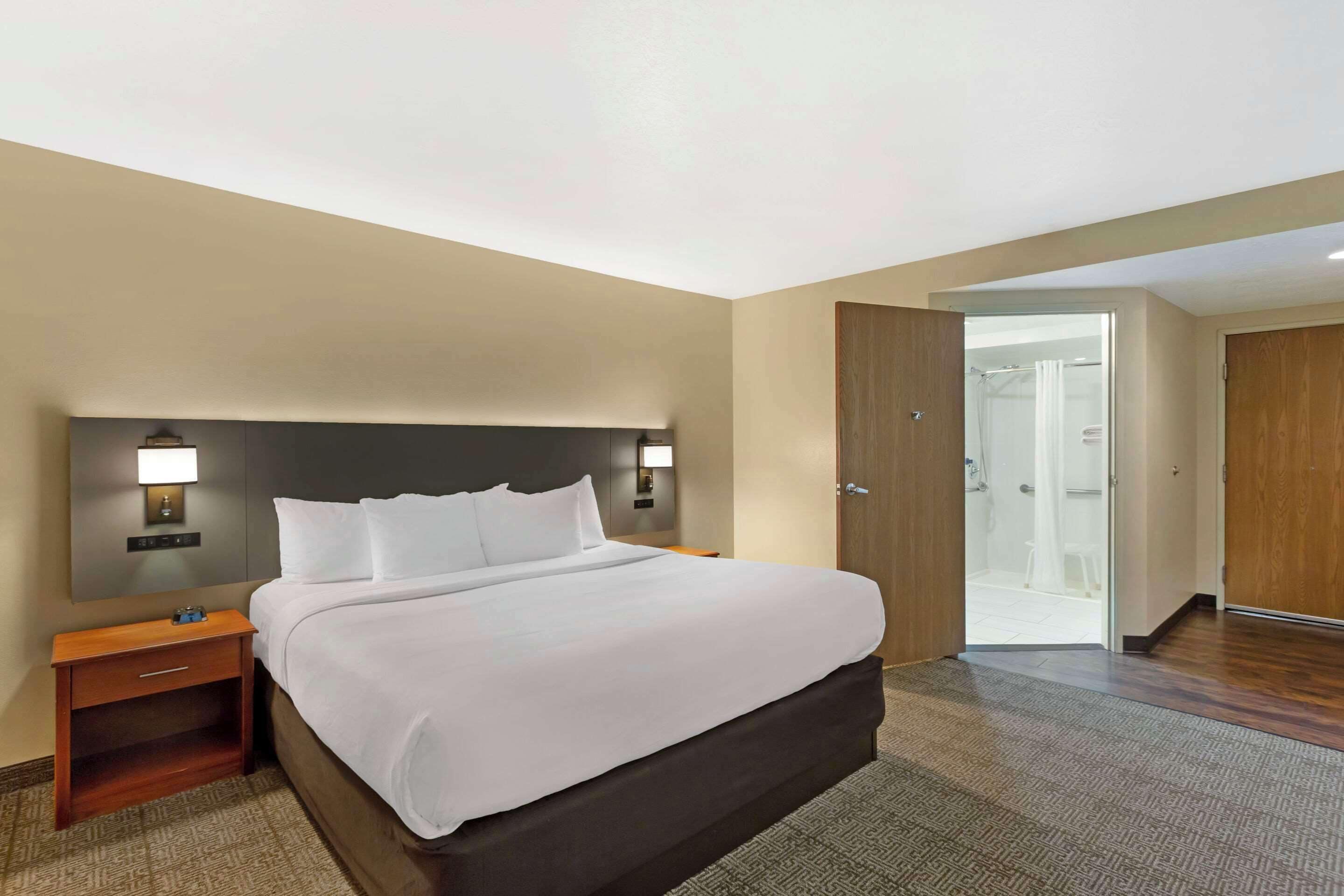 A hotel room with a large bed, bedside tables with lamps, a wooden door, and a bathroom visible through an open door.