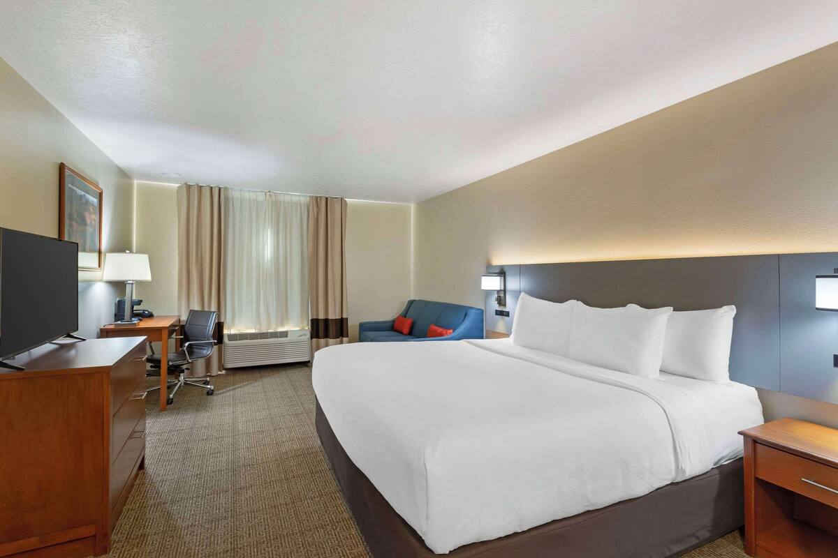 Une chambre d’hôtel avec un grand lit, un bureau avec une chaise, une télévision et un canapé bleu.