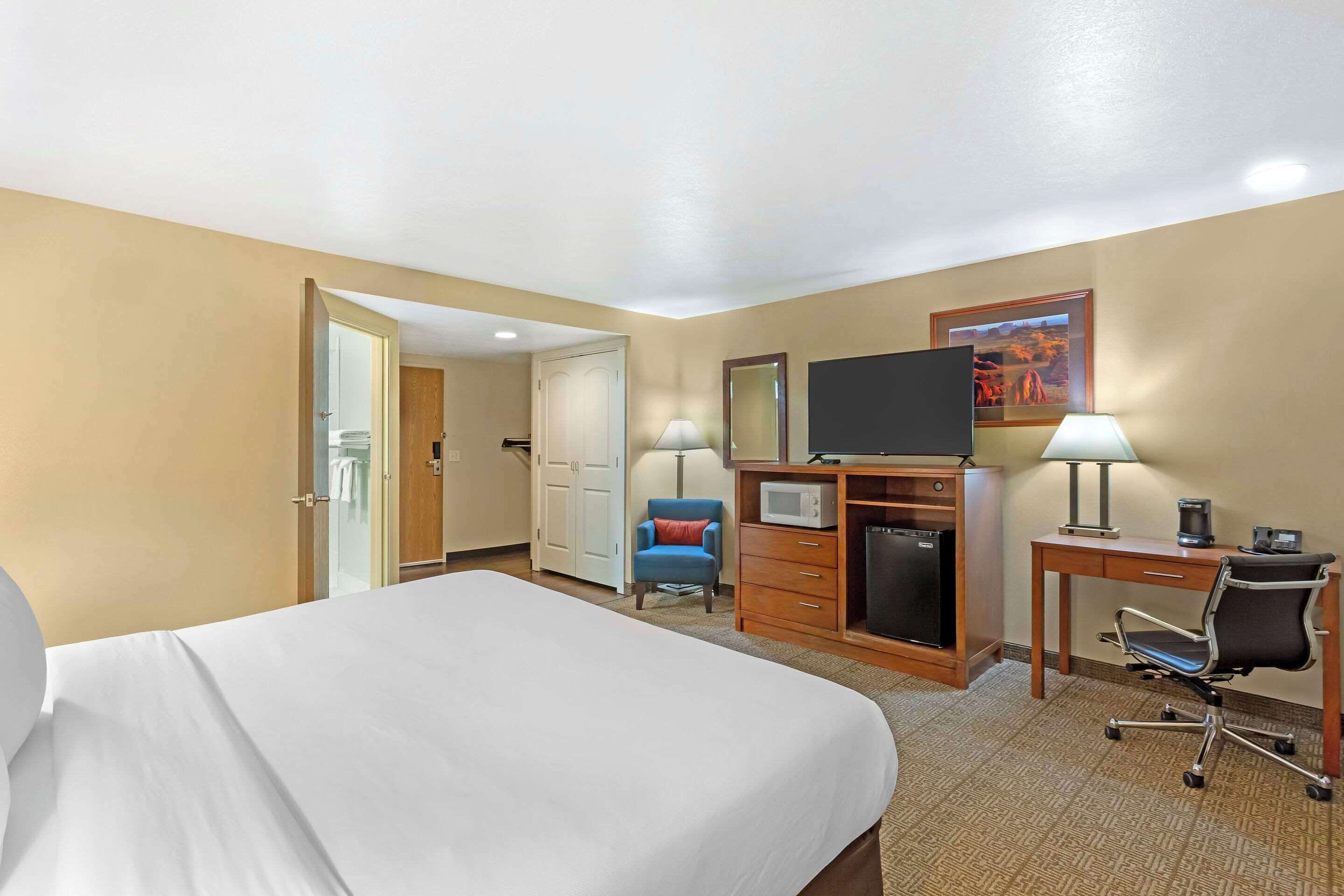 A hotel room with a bed, a desk with a computer, a TV, a microwave, and a chair.