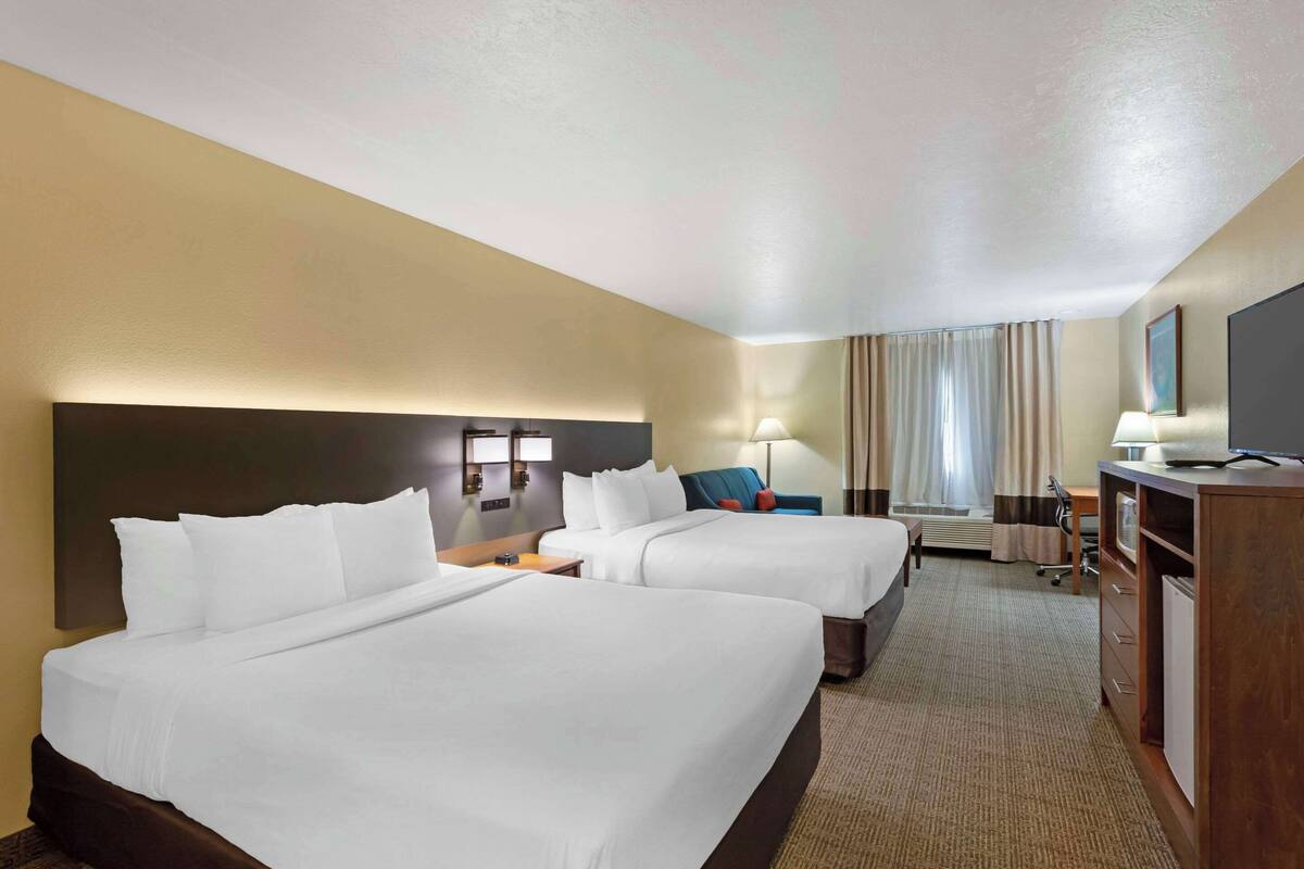 Une chambre d’hôtel avec deux lits, un bureau, une chaise, une télévision et une fenêtre avec des rideaux.