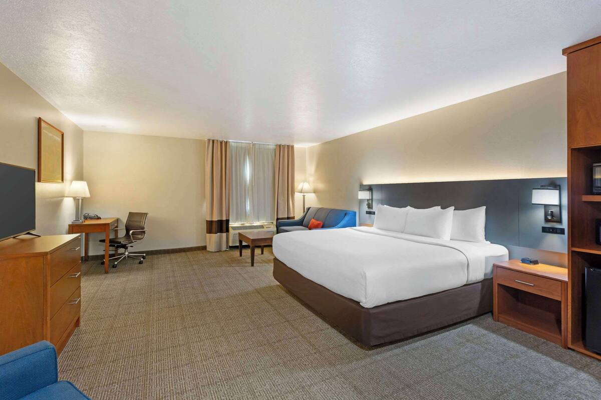 Une chambre d’hôtel avec un grand lit, un bureau, une chaise, une télévision et une armoire.