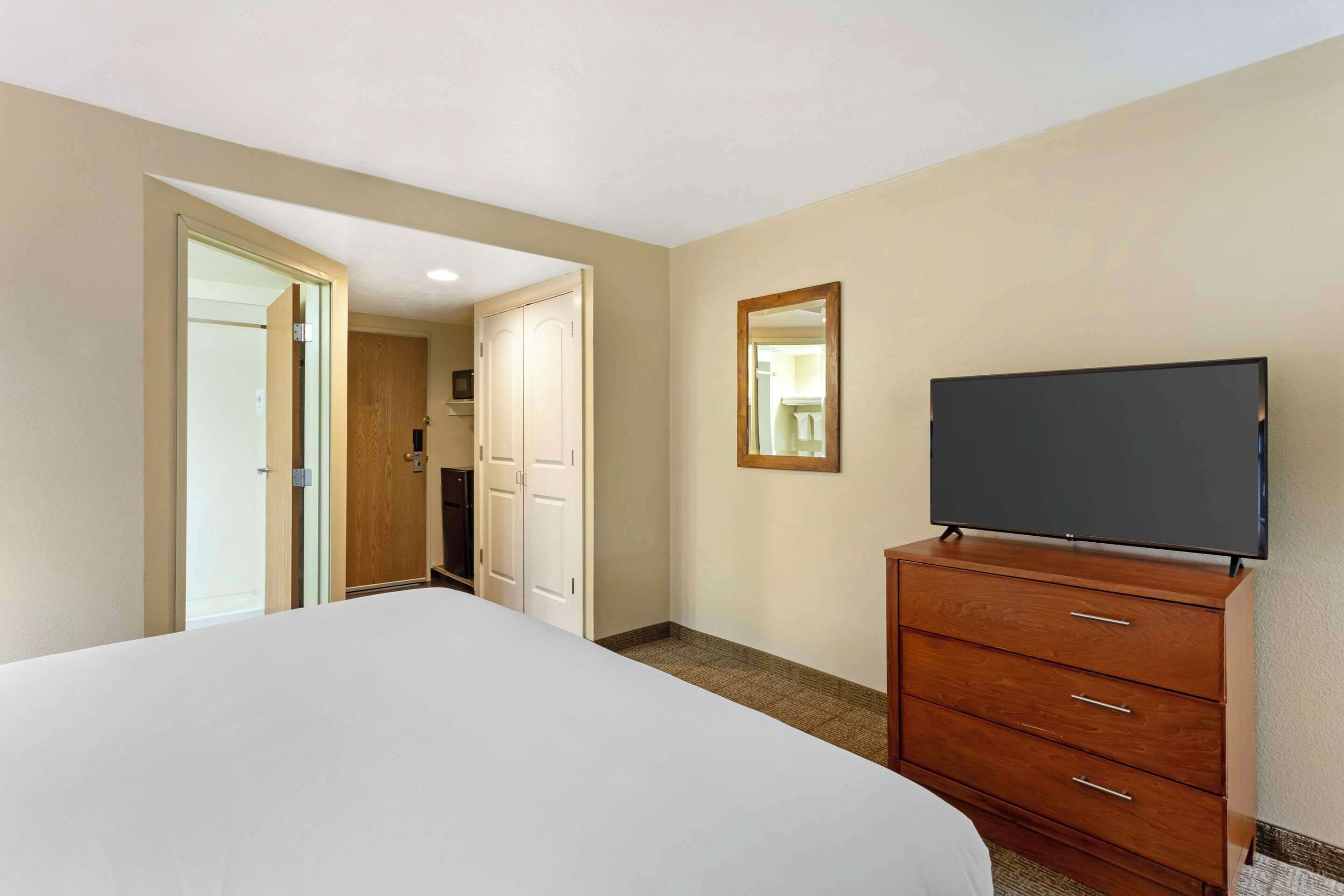 A hotel room with a large bed, a wooden dresser, a flat-screen TV, and a door leading to a bathroom.