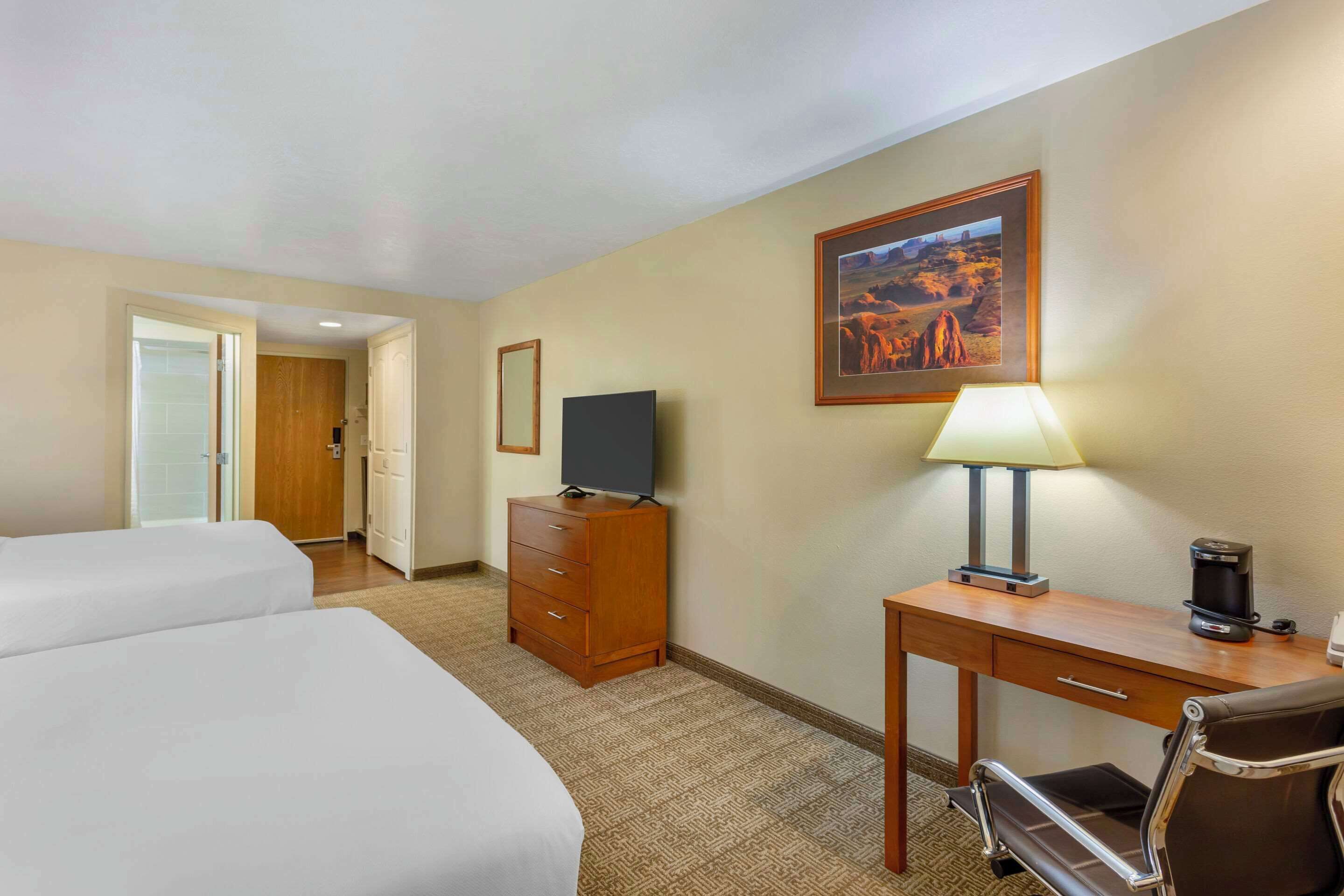 A hotel room with two beds, a desk with a lamp, a coffee maker, and a television.