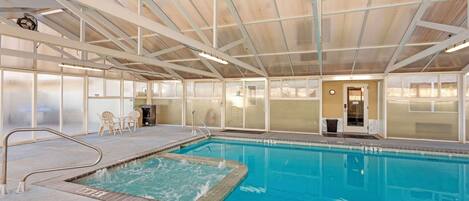An indoor swimming pool with clear water, a diving board, and a covered roof structure.