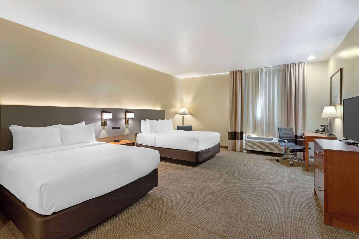 Une chambre d’hôtel avec deux lits, un bureau avec une chaise, une télévision et une grande fenêtre avec des rideaux.