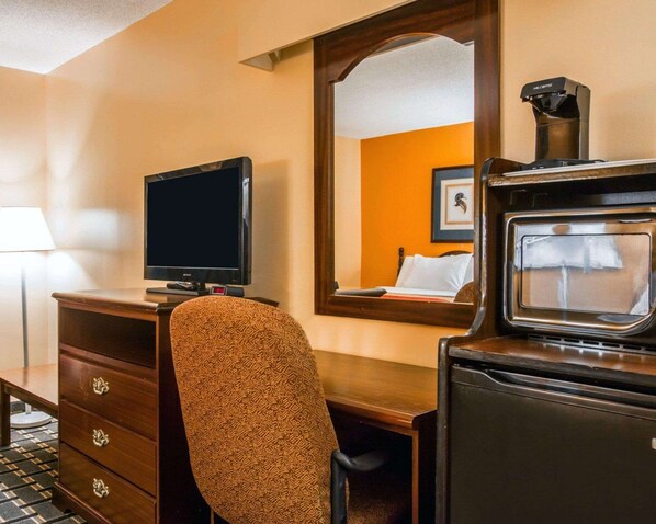 A hotel room with a television, a coffee maker, a desk, and a chair.