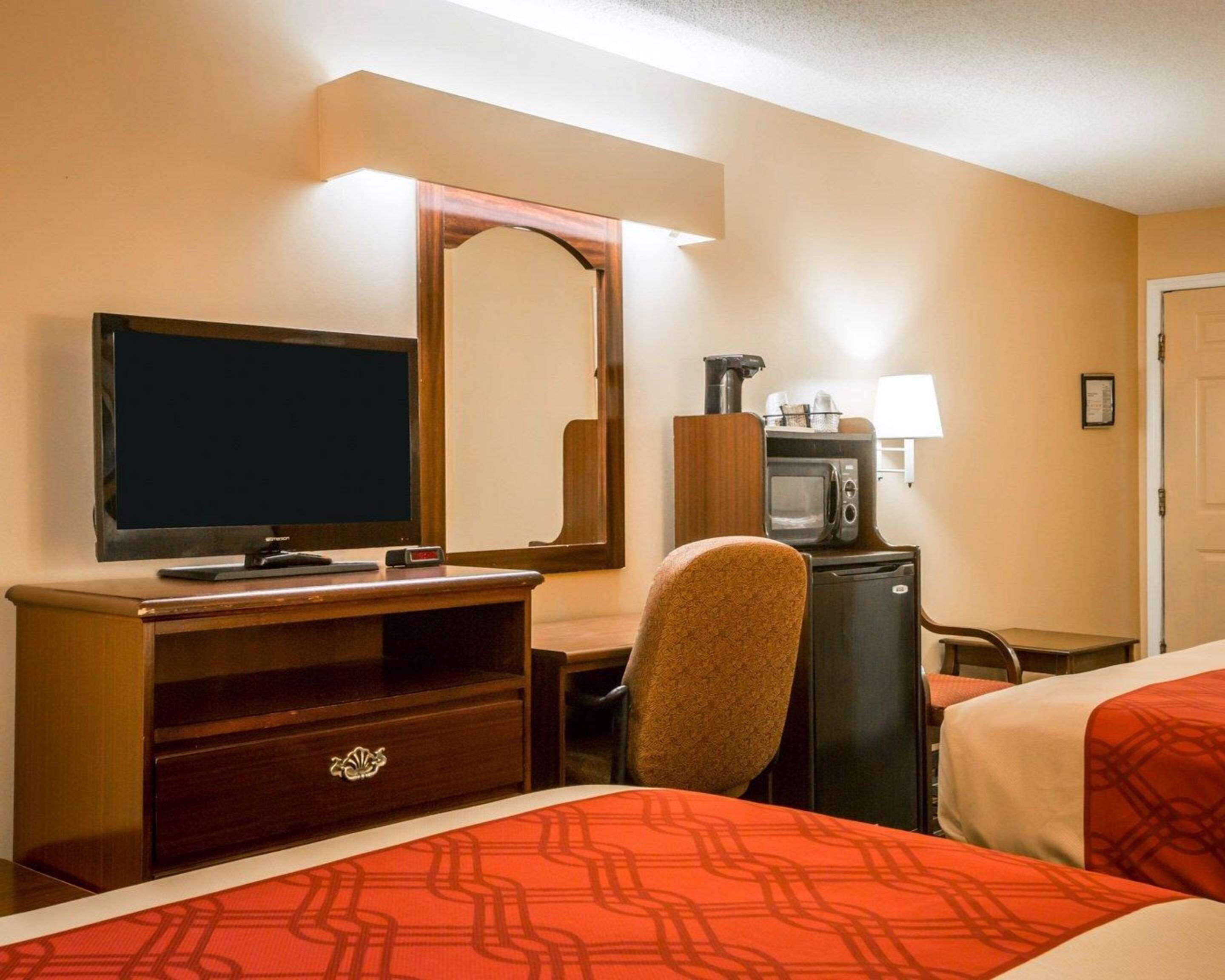 Ein Hotelzimmer mit Fernseher, Schreibtisch mit Lampe, Mikrowelle und zwei Betten mit roter Bettwäsche.