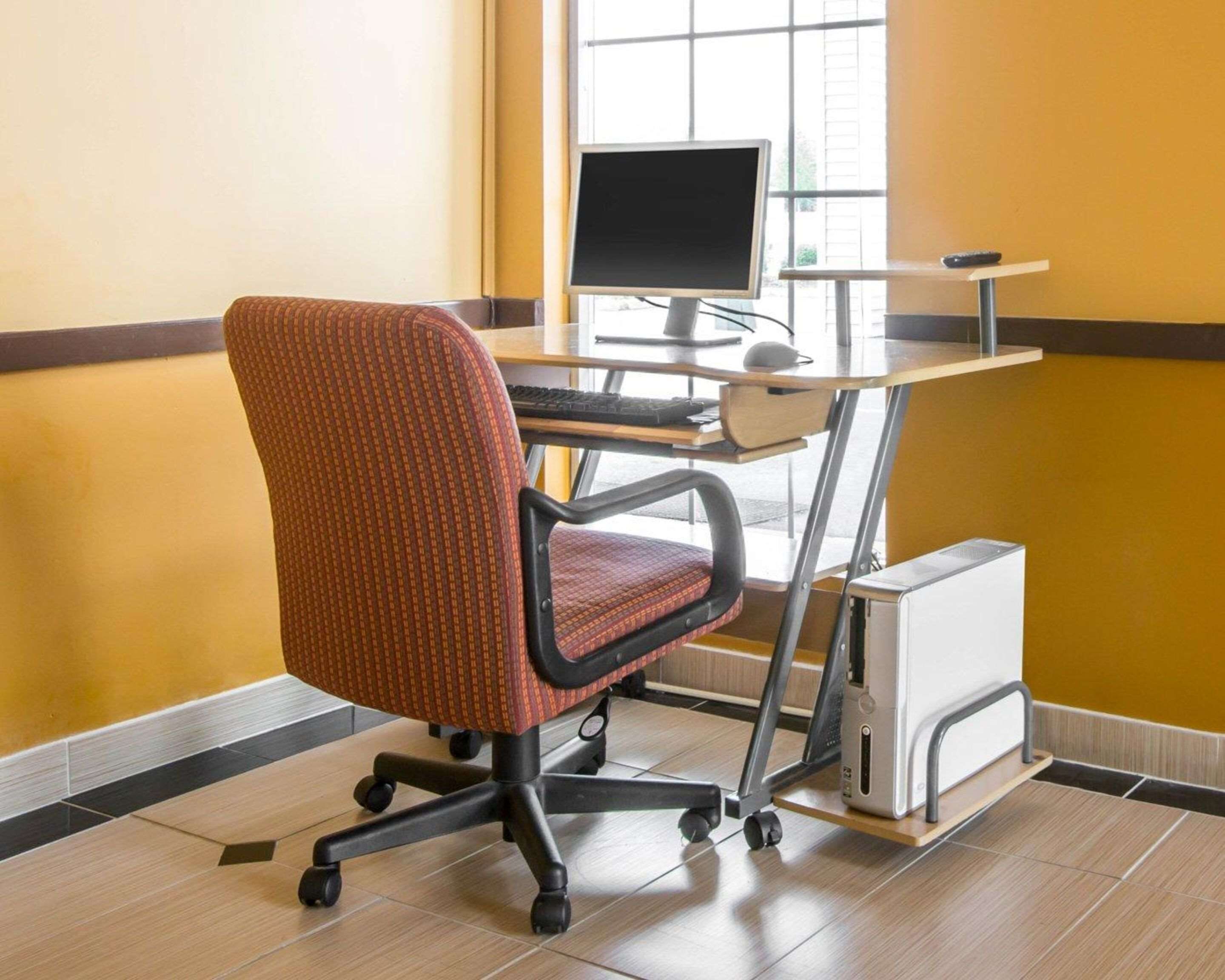 Una moderna sedia da ufficio con ruote, una scrivania con monitor computer, tastiera e mouse, e un piccolo dispositivo bianco su un supporto.