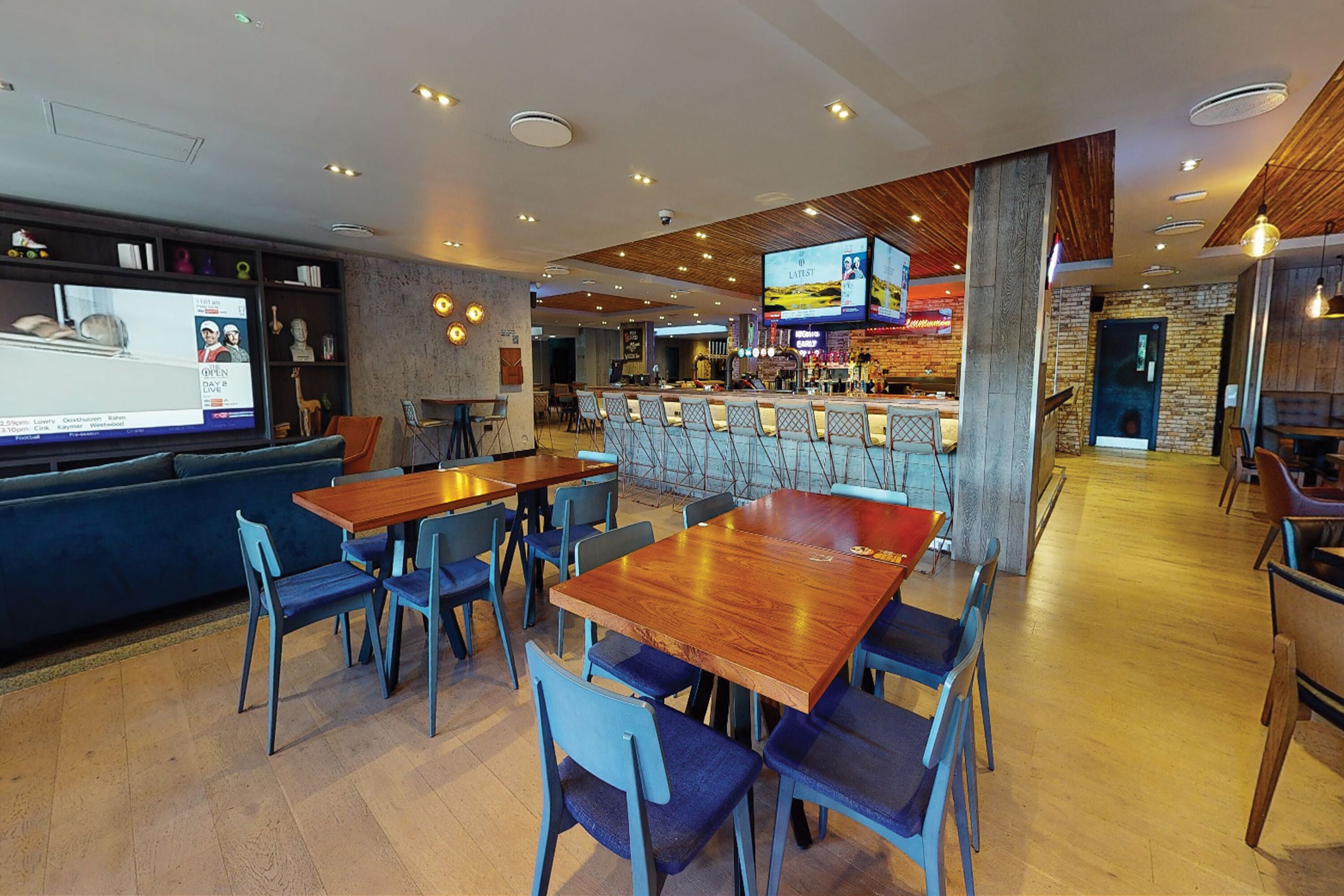 Ein modernes Restaurant mit Holztischen und blauen Stühlen, einer Bar und einem Bildschirm, der eine Speisekarte zeigt.
