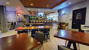 En moderne restaurant med træborde og -stole, et barområde og et tv, der viser en person.