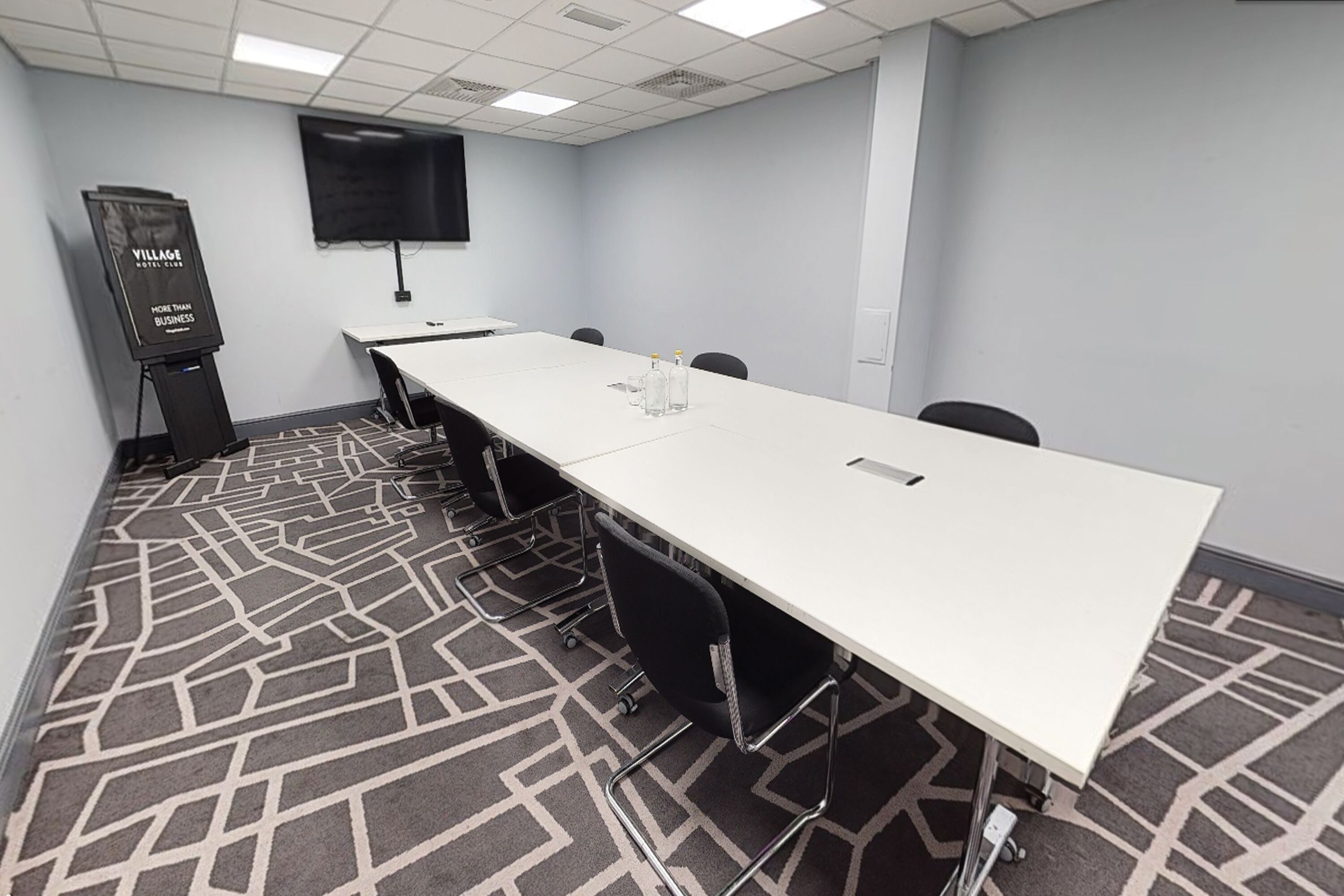 A conference room with a long table, chairs, a projector screen, and a carpeted floor.