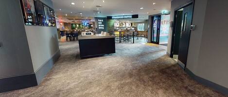 Un vestíbulo de hotel con una recepción central, una cafetería Starbucks y un área de bar.