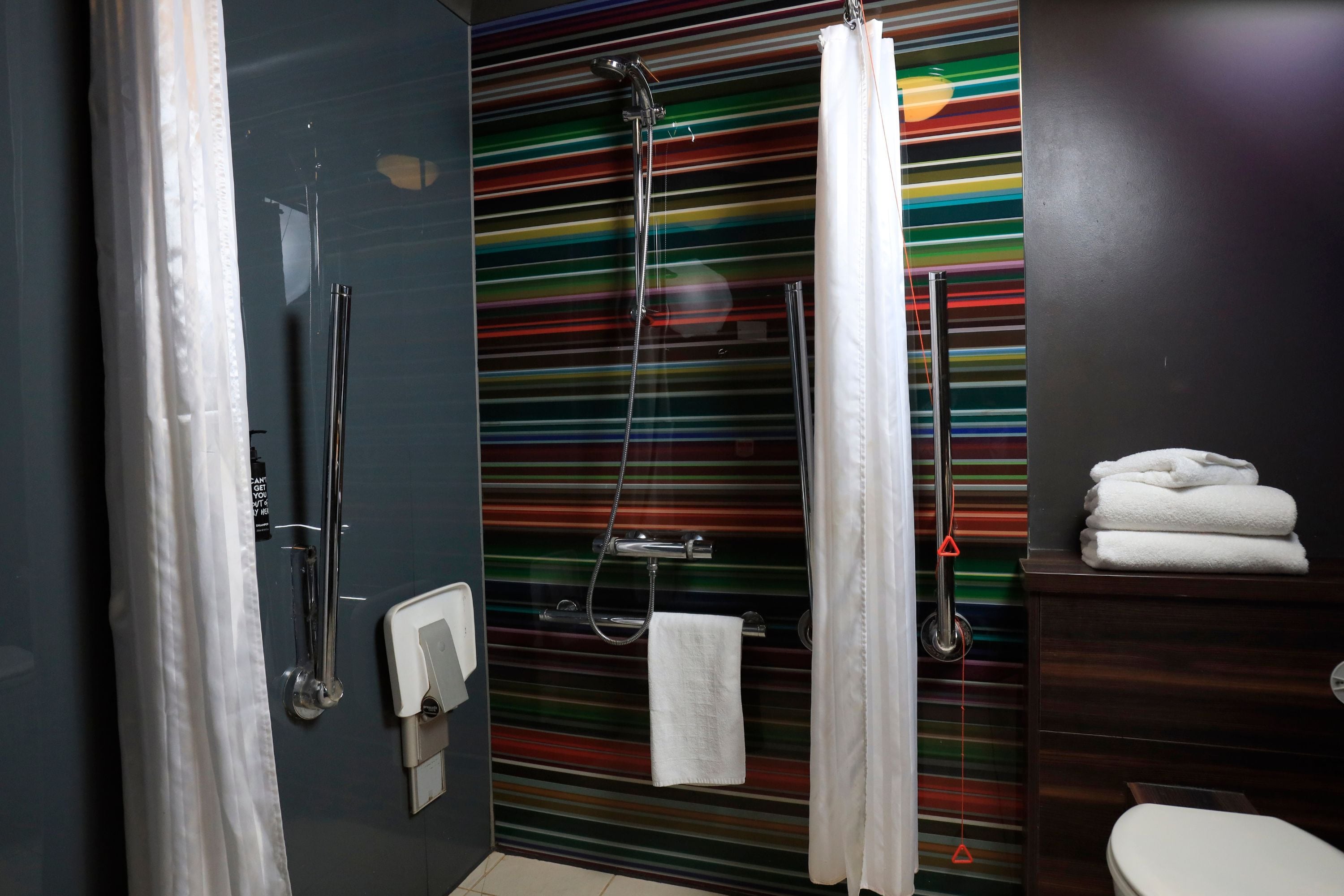 Une salle de bain moderne avec un mur à rayures, une douche, des toilettes et un porte-serviettes.