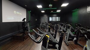 Et fitnesscenter med flere motionscykler og et projektorskærm, der viser "LES MILLS" VIRTUAL.