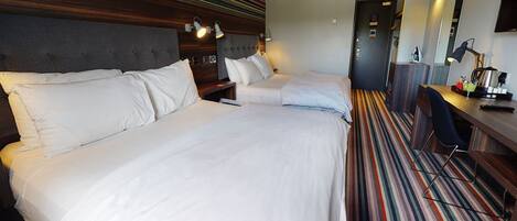 A hotel room with two beds, a desk, a chair, and a striped carpet.