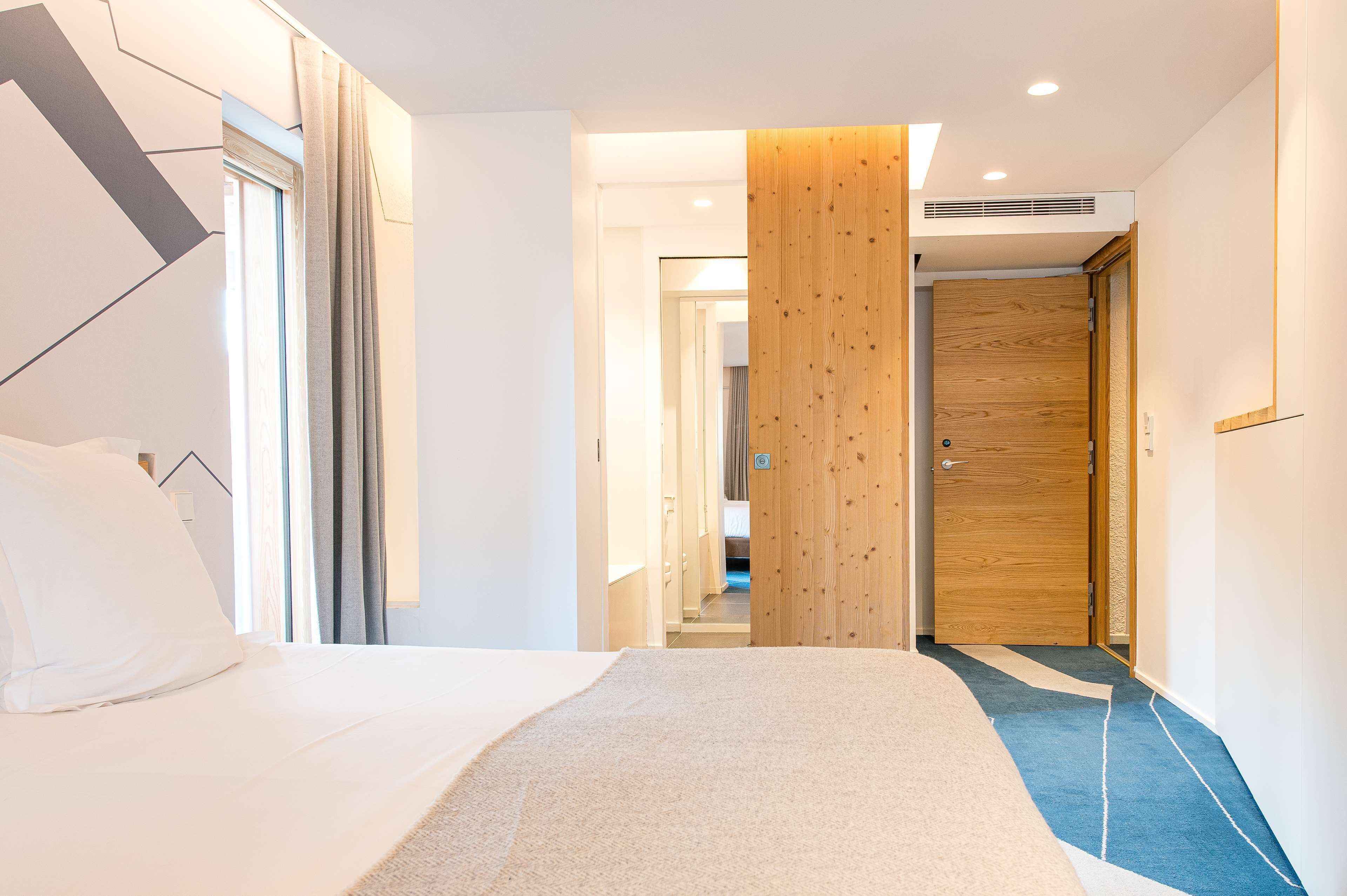 Una habitación de hotel moderna con una cama grande, una puerta de madera y vistas al pasillo.