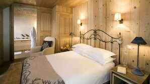 A wooden-paneled room with a bed, two wall-mounted lamps, a nightstand with a book and a glass, and a chair with a pillow. - Hotel Chalet Les Saytels, BW Signature Collection (Le Grand-Bornand)