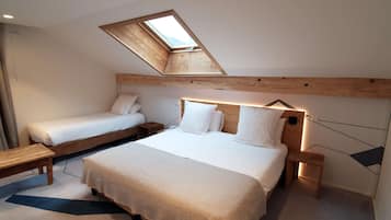 Een slaapkamer met een groot bed, een kleiner bed, een dakraam, een houten hoofdbord, nachtkastjes en een bankje.