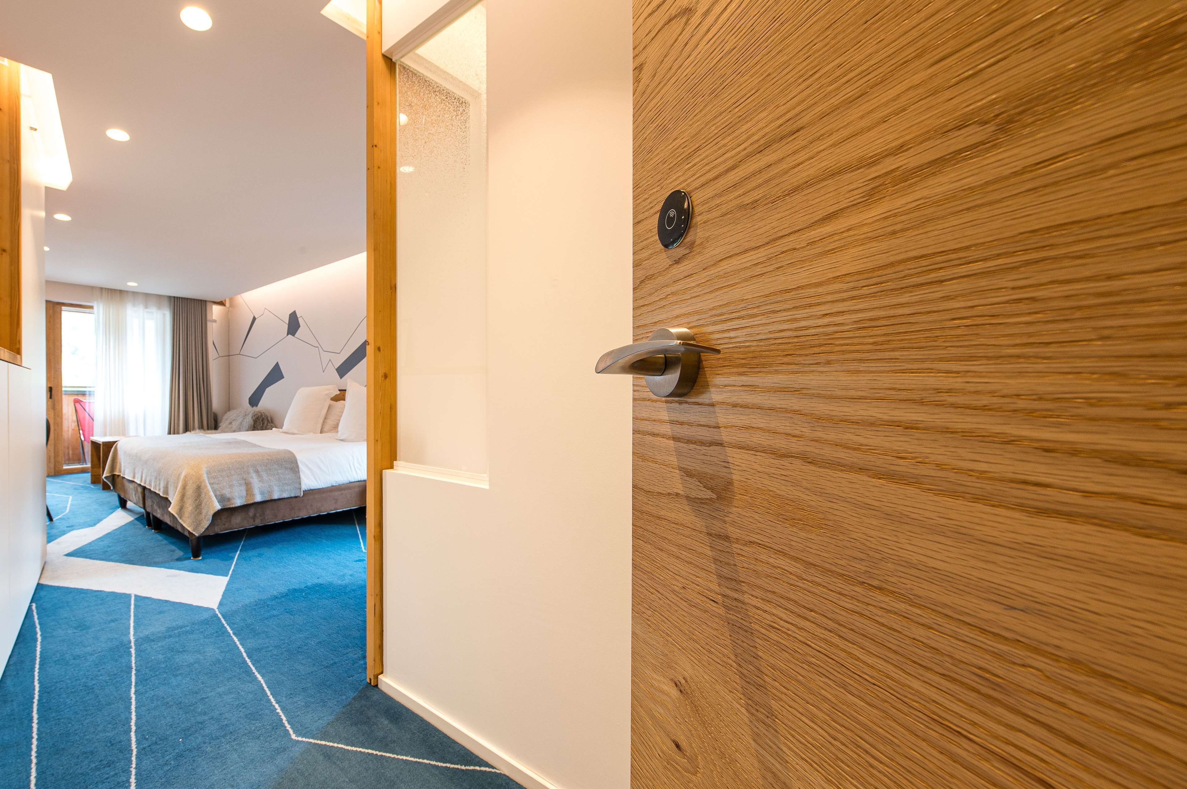 A modern hotel room with a bed, a wooden door, and a blue carpet.