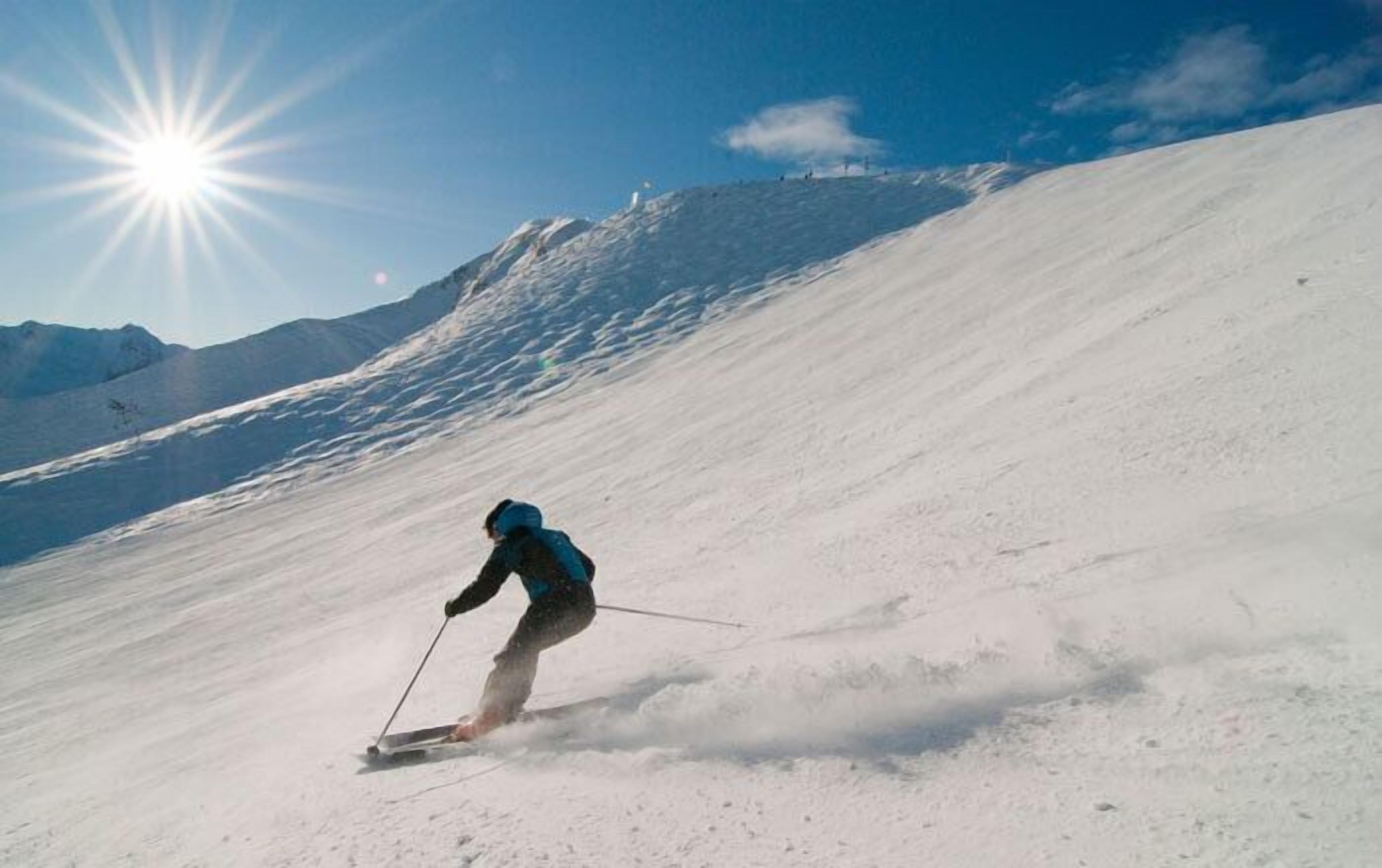A skier on a snowy slope with a clear sky and sun.