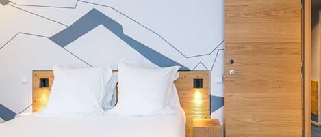Una cama bien tendida con ropa blanca, cabecera de madera y una lámpara fijada a la pared.