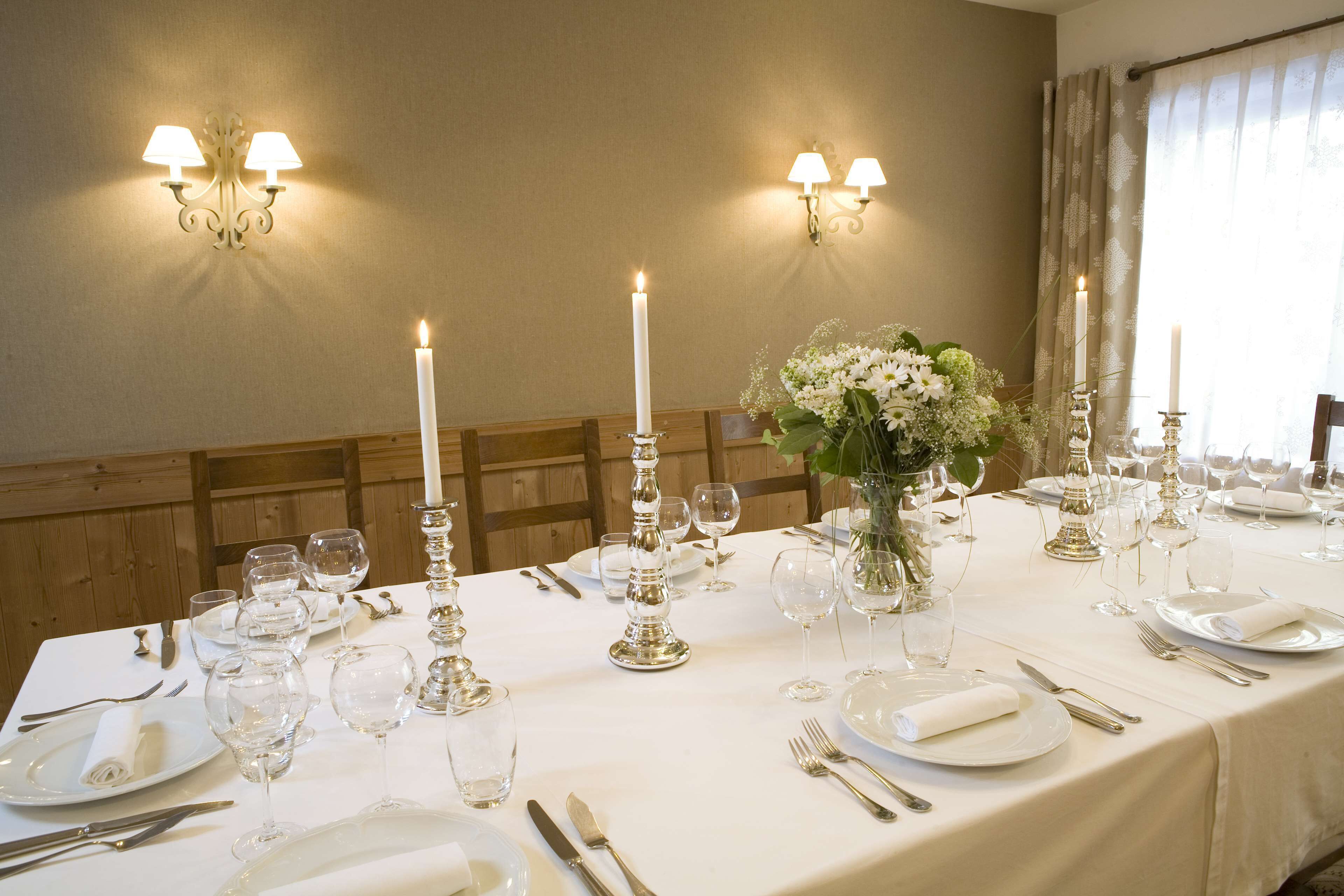Une table à manger élégante, dressée avec des bougies, de la verrerie et des couverts en argent, agrémentée d’appliques murales et d’un arrangement floral au centre.