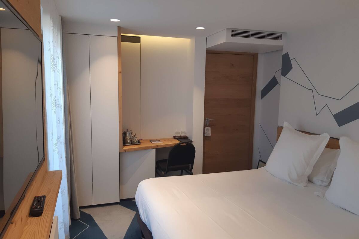 Habitació d'hotel amb llit, escriptori, cadira, armari i mirall.