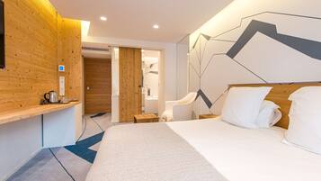 Une chambre d’hôtel moderne avec un mur d’accent en bois, un lit avec du linge de maison blanc, un petit coin salon et une œuvre d’art murale aux motifs géométriques.