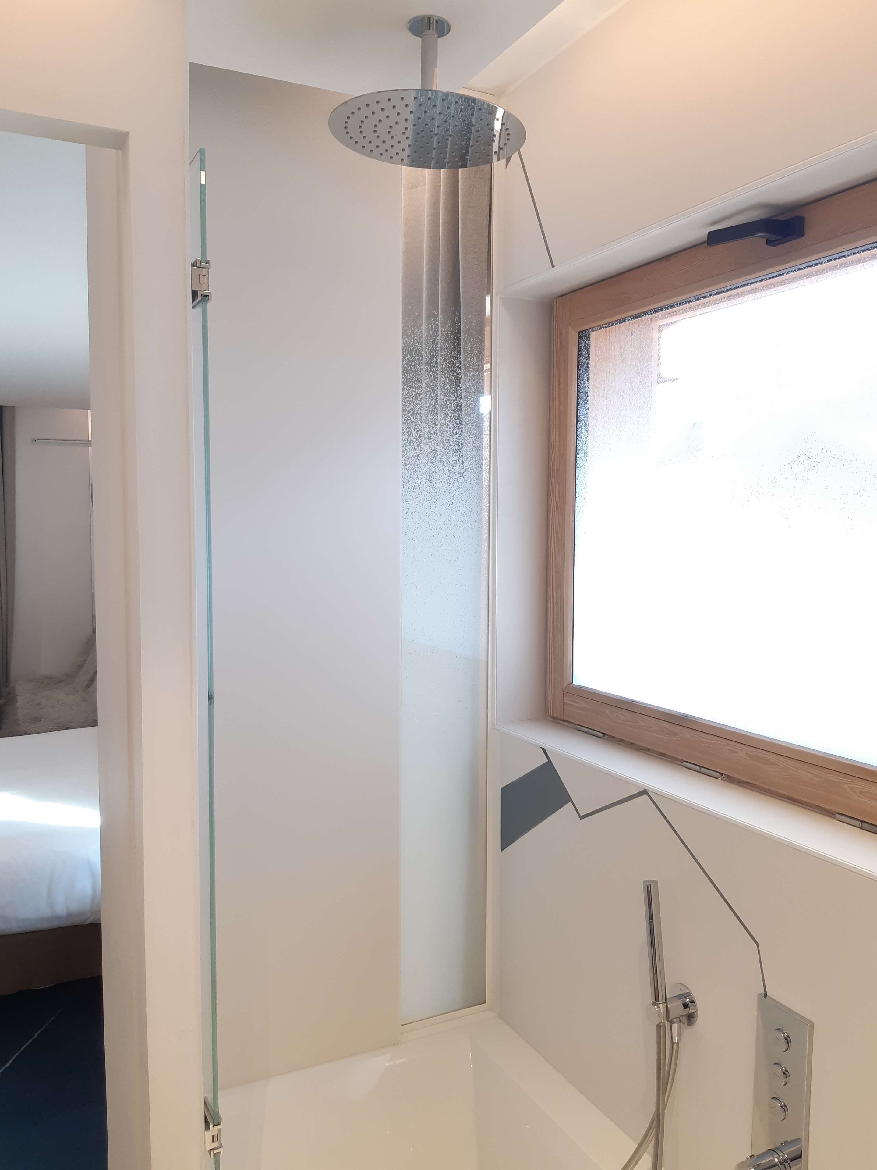 A modern bathroom with a glass shower enclosure, a bathtub, and a window providing natural light.