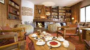 A cozy room with a fireplace, bookshelves, and a dining table set with food and drinks. - Hotel Chalet Les Saytels, BW Signature Collection (Le Grand-Bornand)