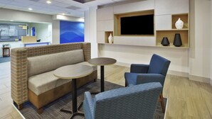 A modern hotel lobby with a sofa, chairs, a TV, and a reception desk. - Holiday Inn Express & Suites Manchester by IHG (Manchester)