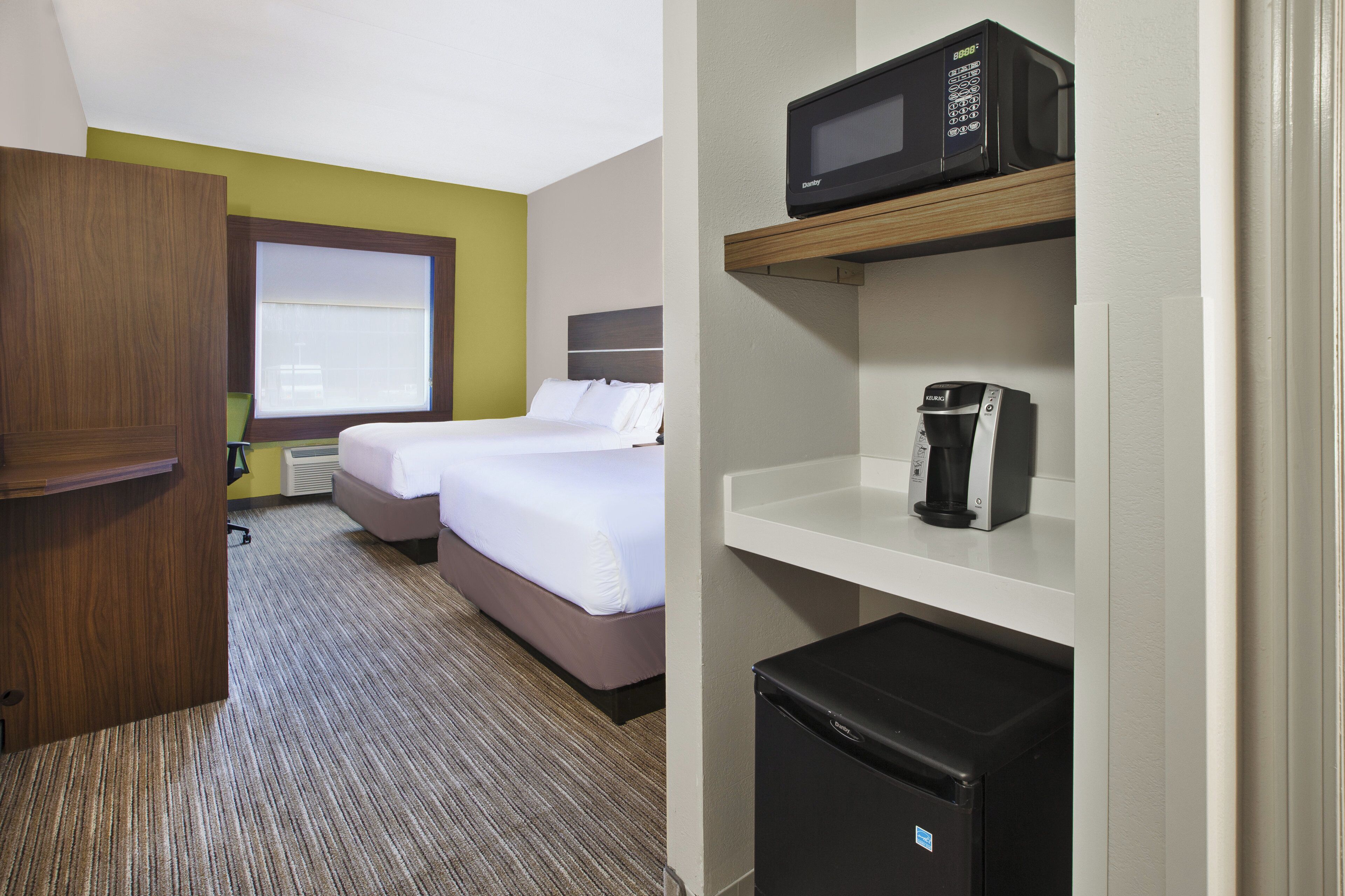 Habitación de hotel con una cama, microondas, cafetera y refrigerador.