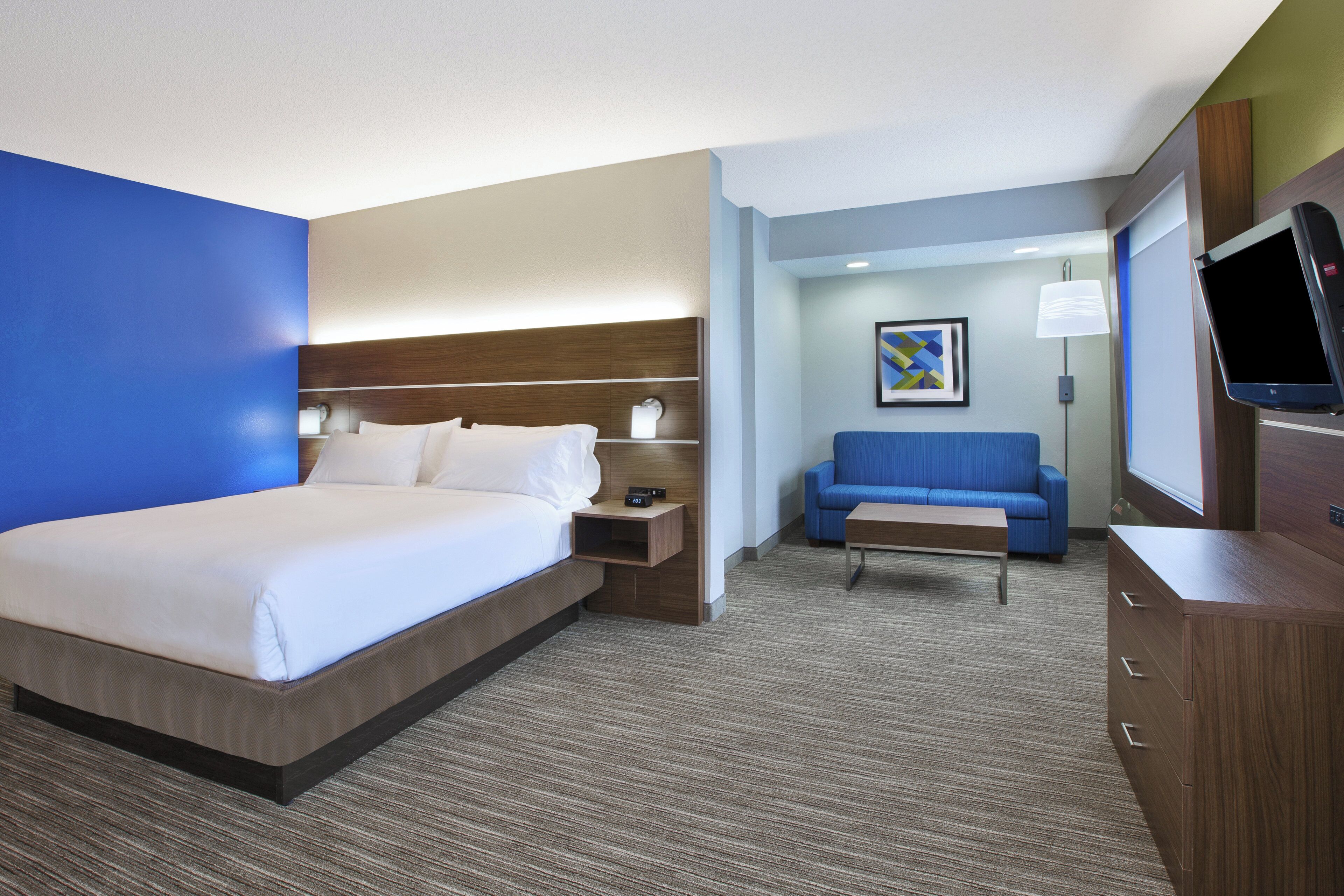 A hotel room with a bed, a nightstand, a seating area with a sofa, a small table, and a TV.