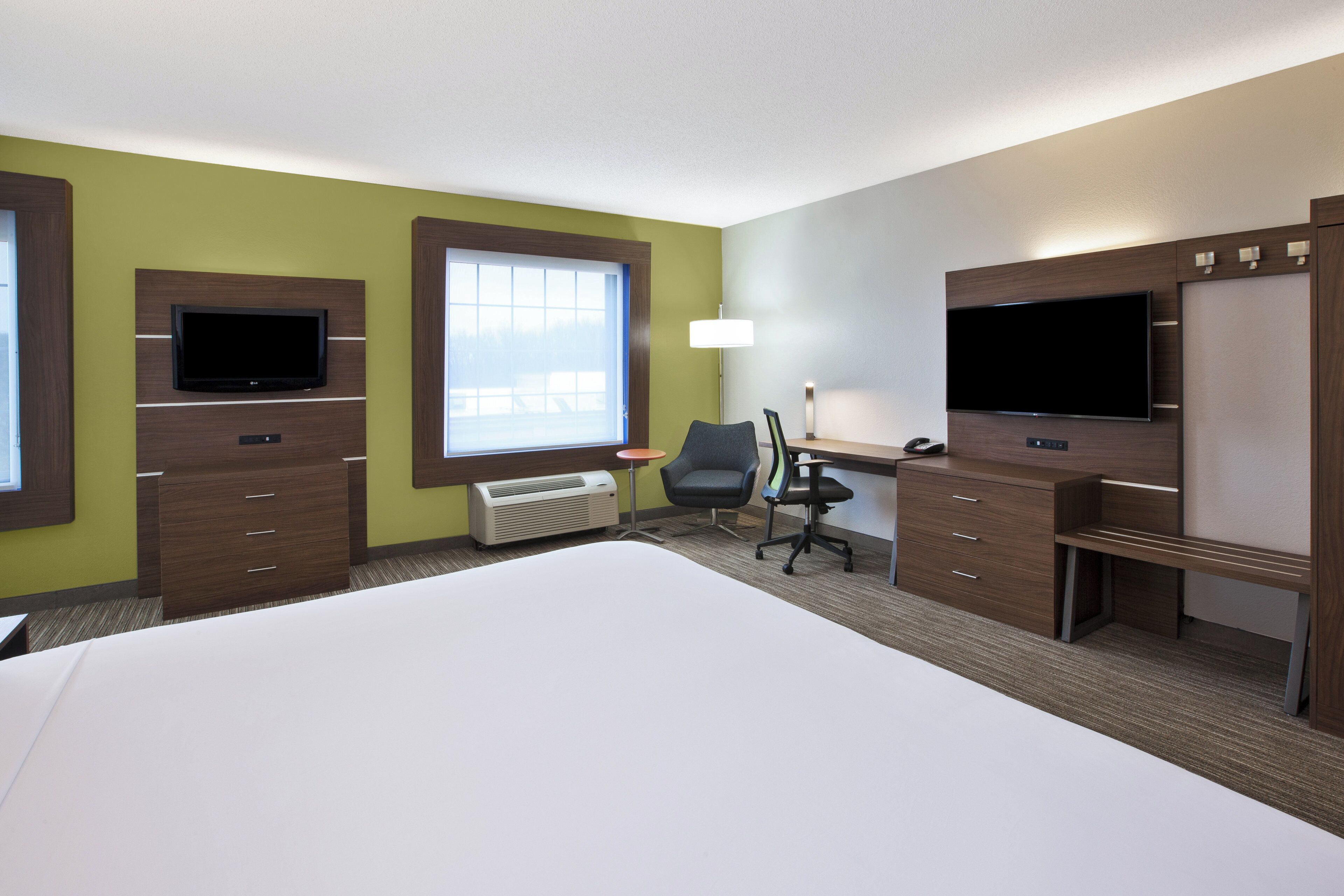 A hotel room with a bed, a desk, a chair, a TV, and a window.