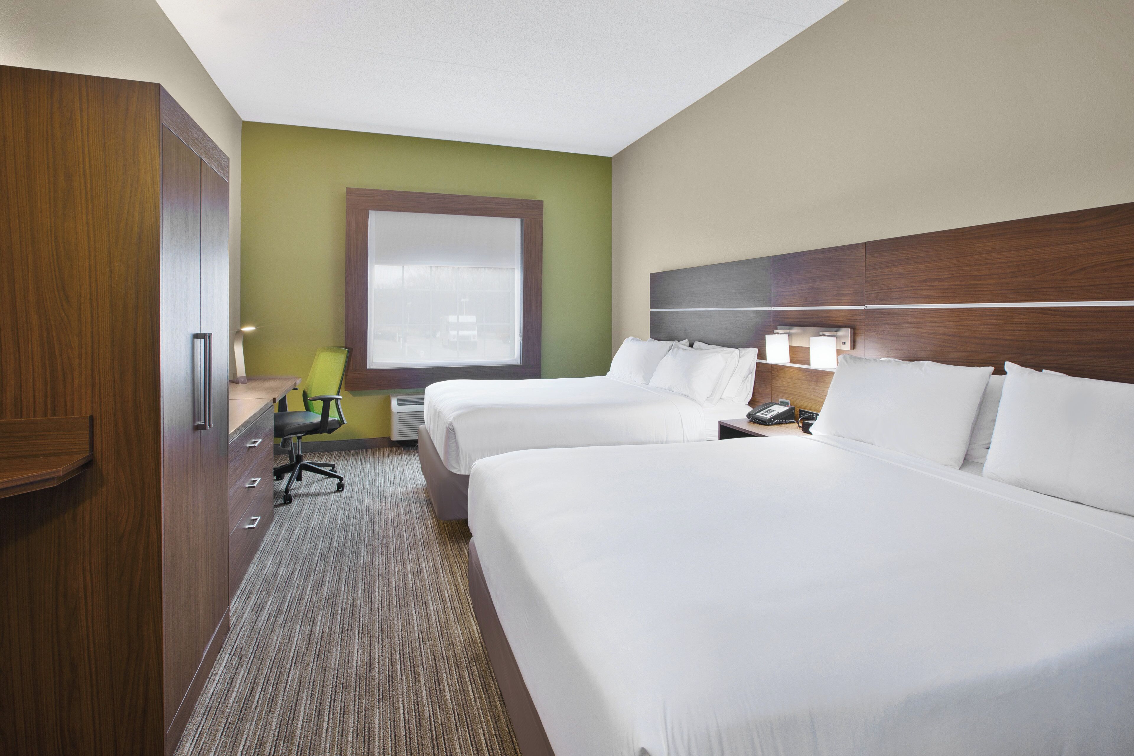 A hotel room with two beds, a desk, a chair, and a window.