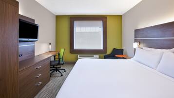 Quarto de hotel com uma cama, escrivaninha, cadeira, televisão e janela.